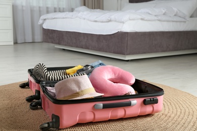 Photo of Opened suitcase with clothes and travel pillow in bedroom