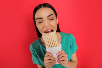 Photo of Young woman eating delicious shawarma on red background