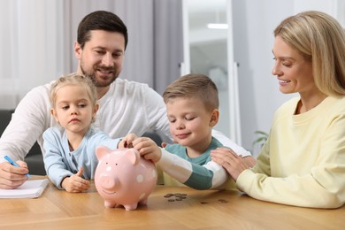 Photo of Family budget. Children putting coins into piggy bank while their parents watching at them indoors
