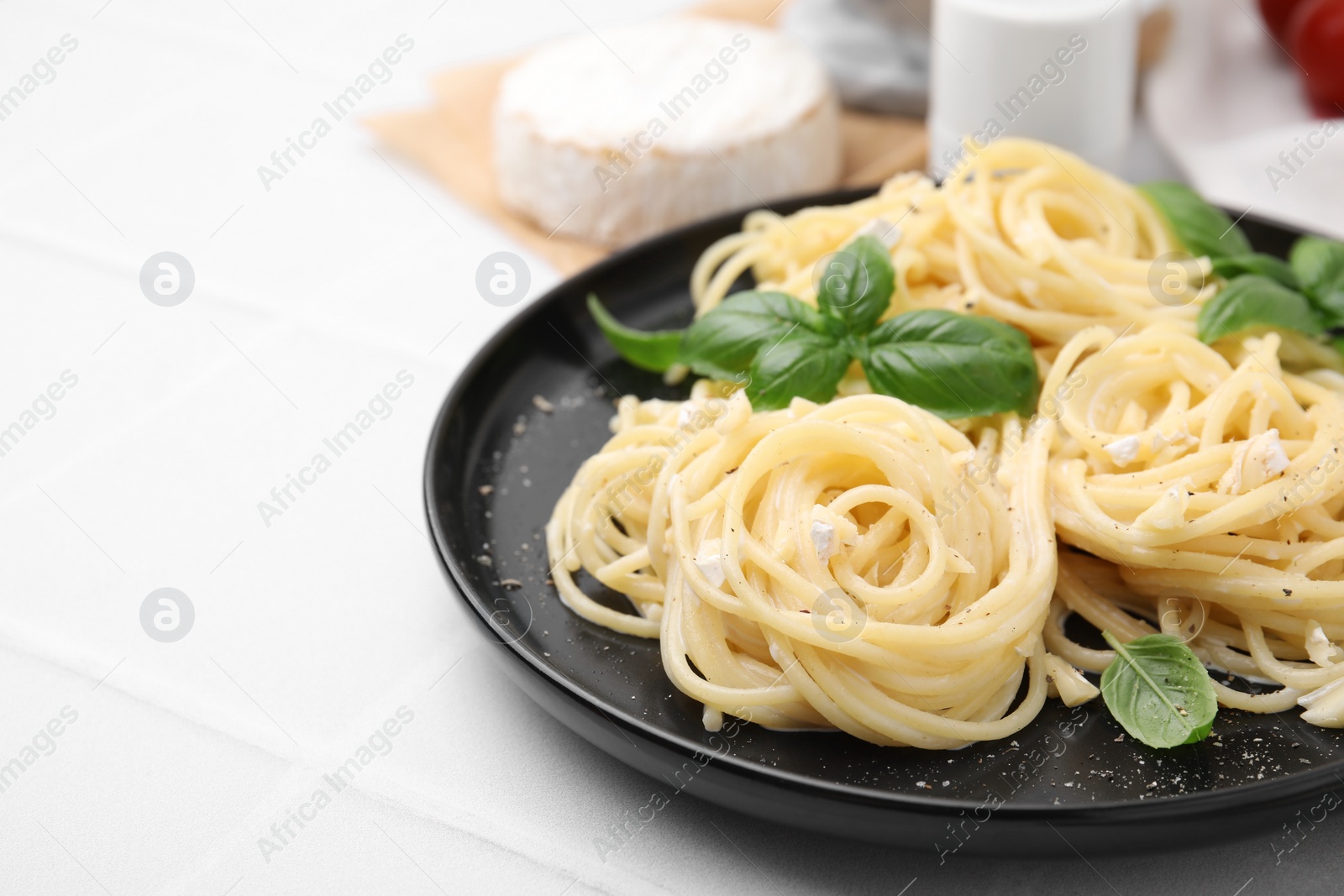 Photo of Delicious pasta with brie cheese and basil leaves on white tiled table, closeup. Space for text