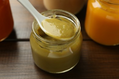 Eating baby food with spoon at wooden table, closeup