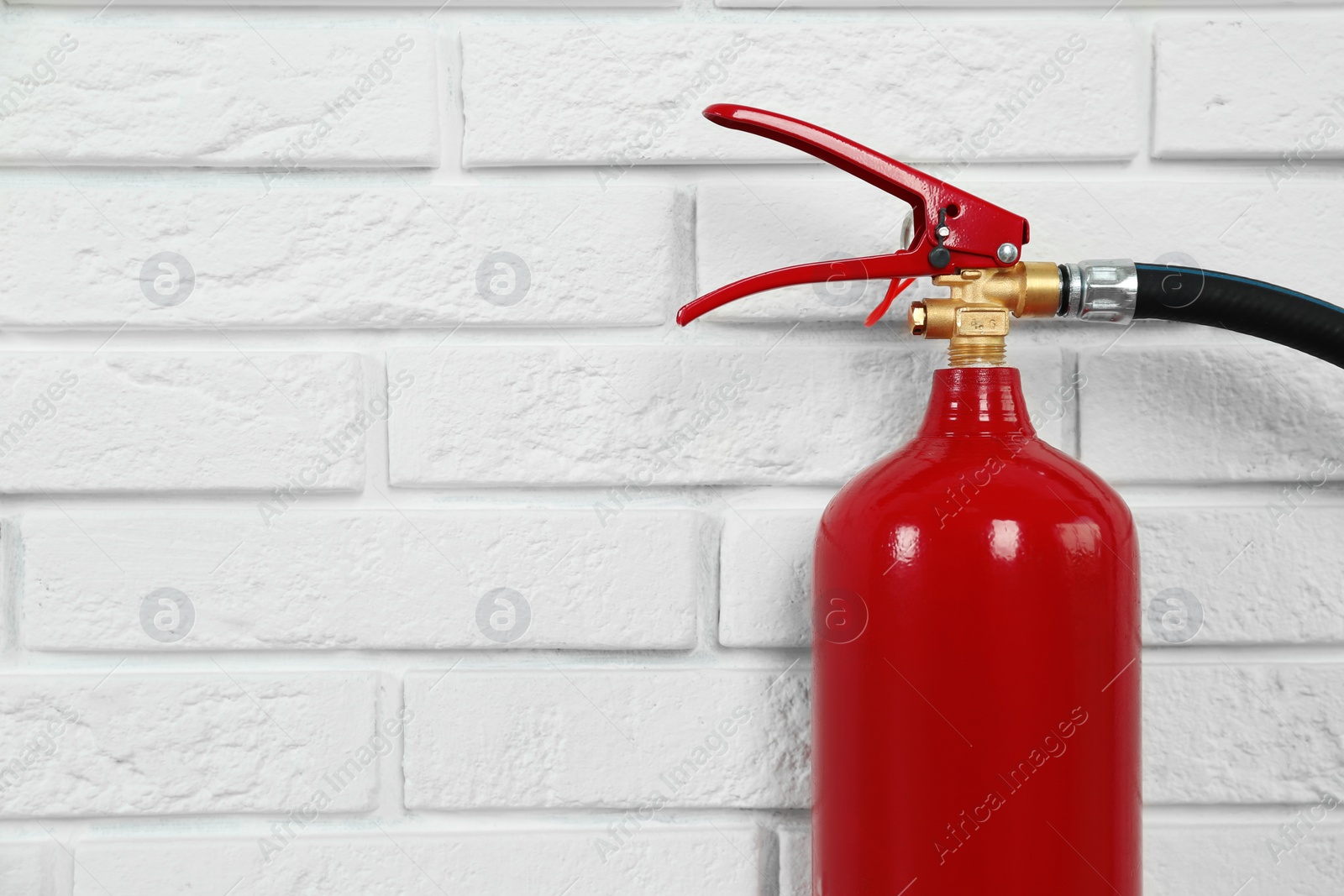 Photo of Fire extinguisher near white brick wall, closeup. Space for text