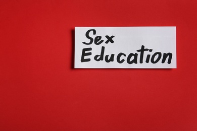 Photo of Piece of paper with phrase "SEX EDUCATION" on red background, top view, Space for text