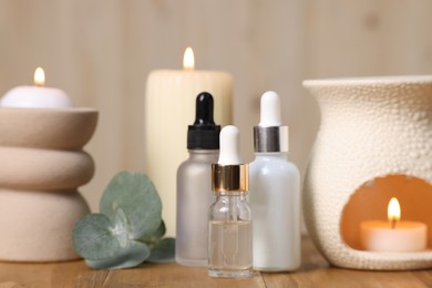 Different aromatherapy products, burning candles and eucalyptus leaves on wooden table, closeup