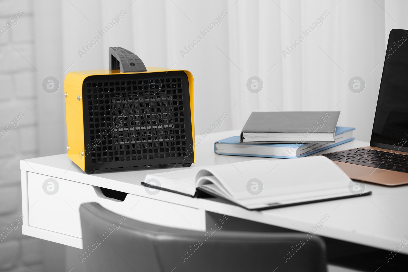 Photo of Modern electric fan heater near notebooks on white table in office