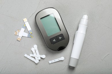 Photo of Glucometer, lancet pen and strips on grey table, flat lay. Diabetes testing kit