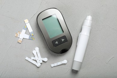 Glucometer, lancet pen and strips on grey table, flat lay. Diabetes testing kit