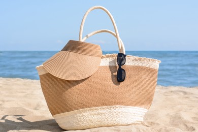 Photo of Stylish straw bag with visor cap and sunglasses on sandy beach near sea