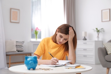 Sad woman with piggy bank and money at table indoors