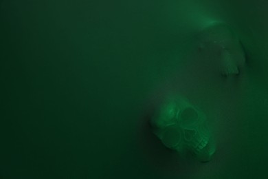 Photo of Silhouette of creepy ghost with skulls behind green cloth. Space for text