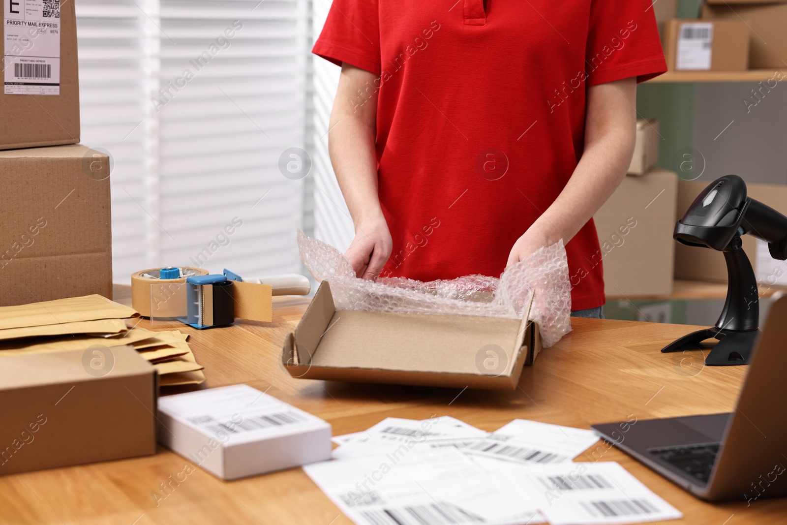 Photo of Post office worker packing parcel at wooden table indoors, closeup