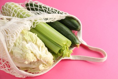 Photo of String bag with different vegetables on bright pink background, closeup