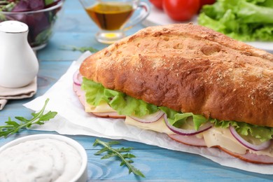 Photo of Delicious sandwich with fresh vegetables, cheese and arugula on light blue wooden table, closeup
