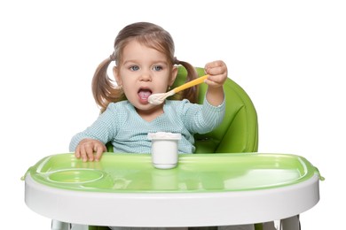 Photo of Cute little child eating tasty yogurt from plastic cup with spoon in high chair on white background