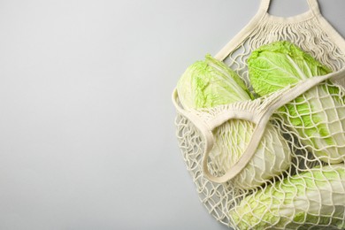 Fresh Chinese cabbages in string bag on light background, top view. Space for text