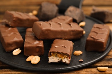 Photo of Slate board of chocolate bars with caramel, nuts and nougat on wooden table, closeup