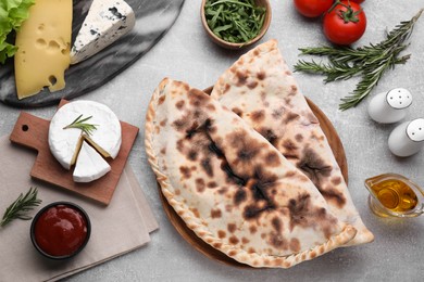 Photo of Tasty pizza calzones with tomato sauce and different products on light grey table, flat lay