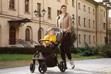 Happy mother walking with her son in stroller outdoors