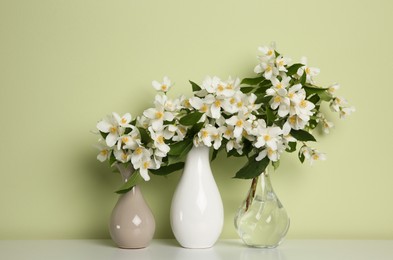 Photo of Beautiful jasmine flowers in vases on table near light green wall