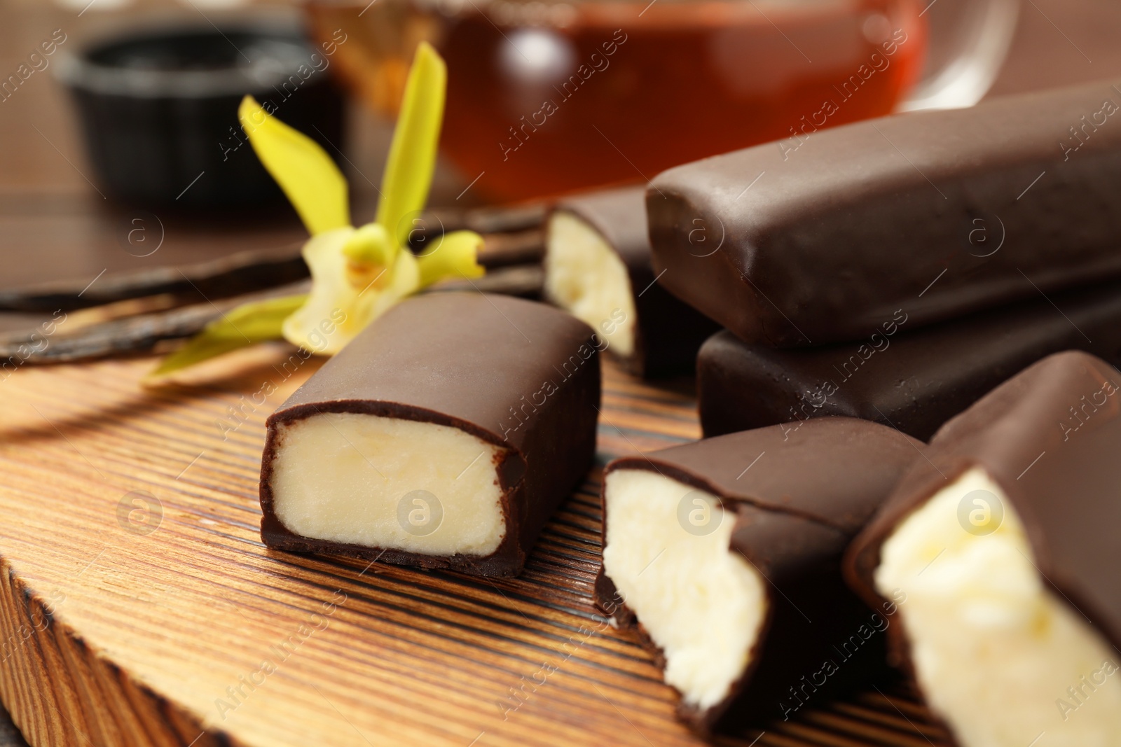 Photo of Glazed curd cheese bars and vanilla flower on wooden table, closeup