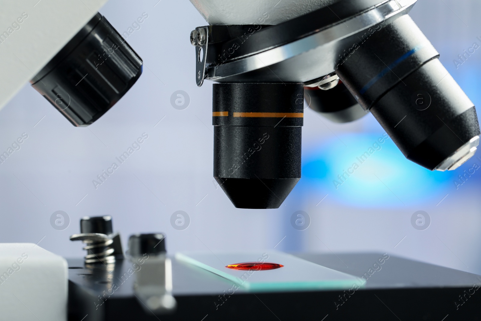 Photo of Glass slide with sample of red liquid under microscope in laboratory, closeup