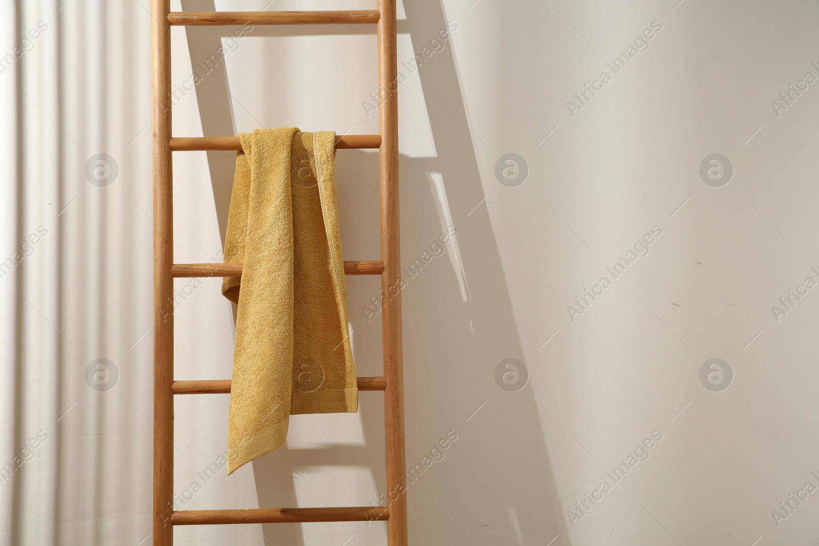 Photo of Yellow towel hanging on wooden ladder indoors. Space for text