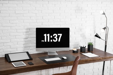 Modern workplace interior with computer and devices on table near brick wall