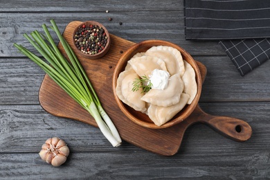 Photo of Bowl of tasty dumplings served on dark wooden table, flat lay