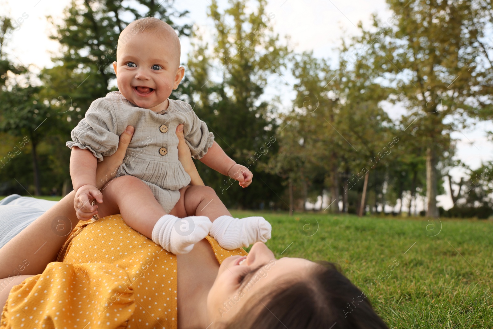 Photo of Happy mother with adorable baby lying on green grass in park