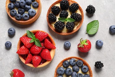 Tartlets with different fresh berries on light grey table, flat lay. Delicious dessert