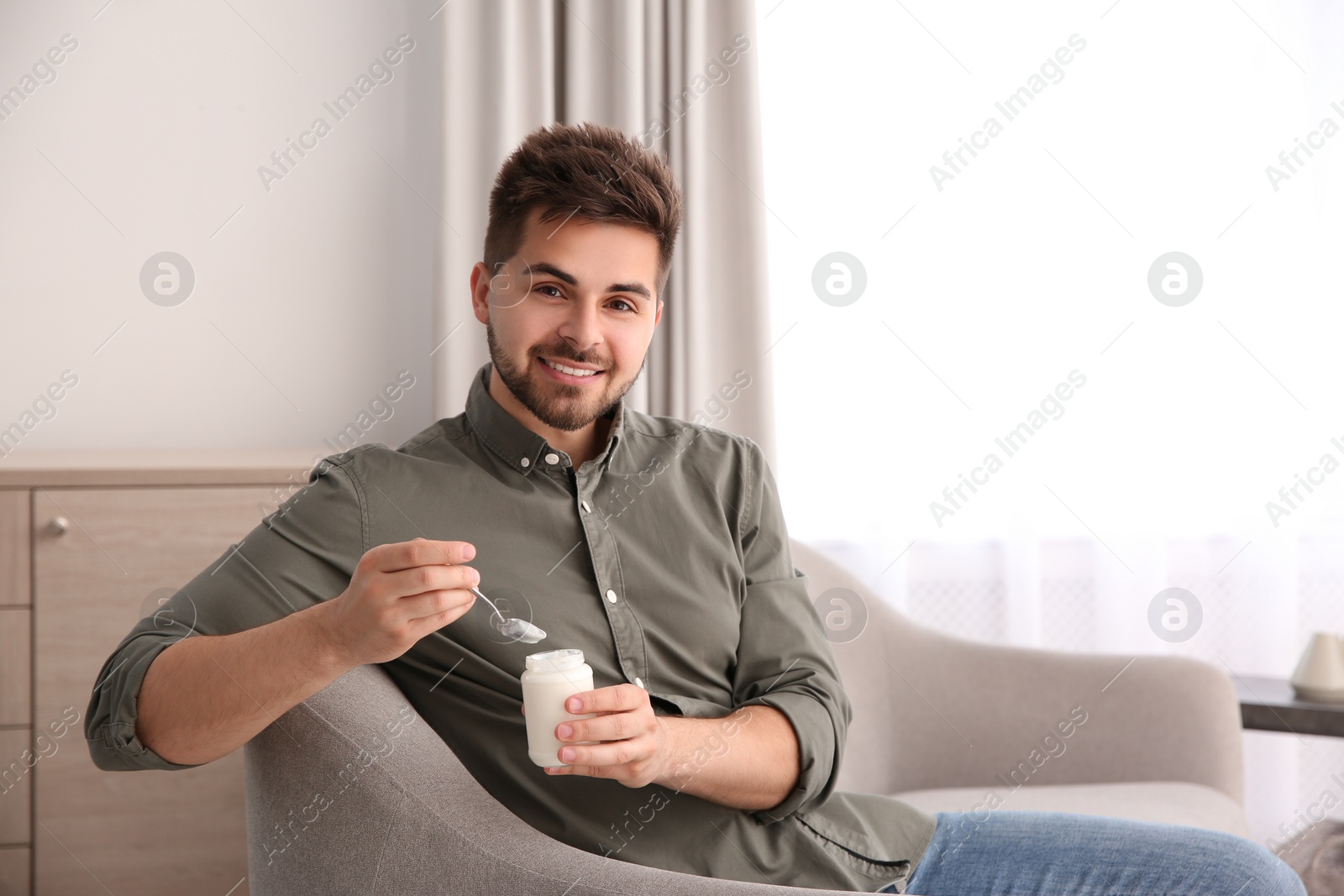 Photo of Happy young man with tasty yogurt in living room. Space for text