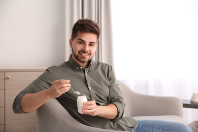 Photo of Happy young man with tasty yogurt in living room. Space for text