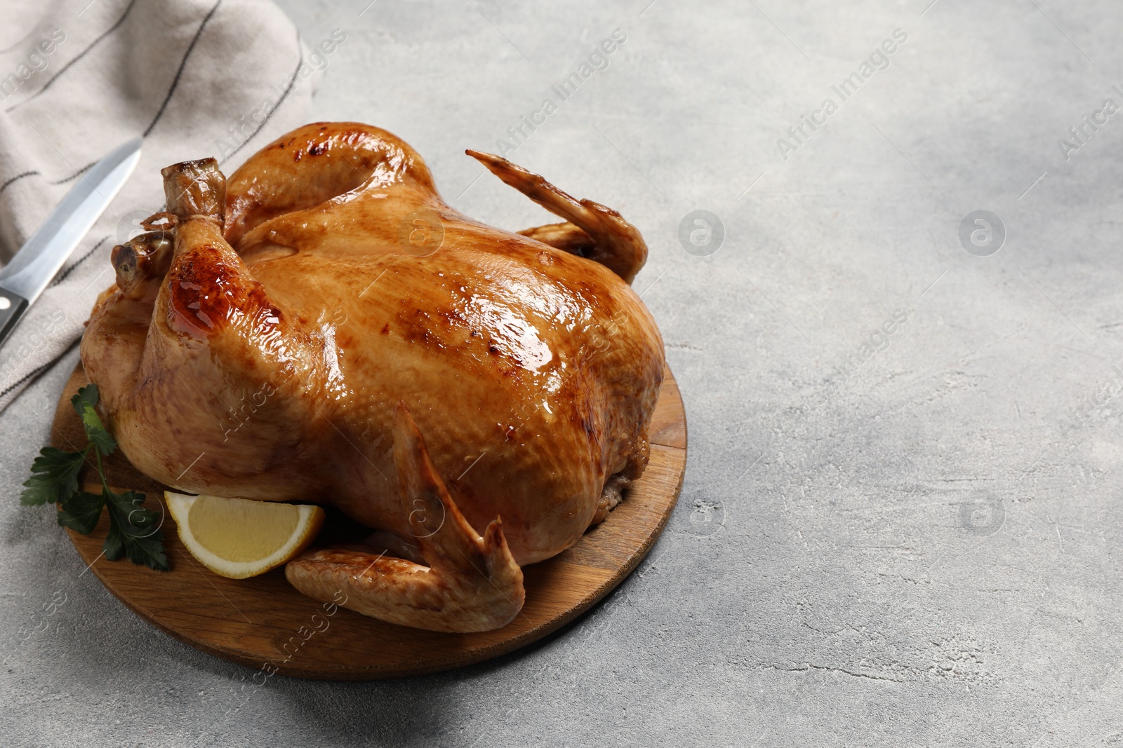 Photo of Tasty roasted chicken with parsley and lemon on light grey table. Space for text