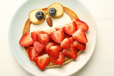 Creative serving for kids. Plate with cute owl made of pancakes, strawberries, cream, banana and almond on white wooden table, top view