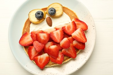 Photo of Creative serving for kids. Plate with cute owl made of pancakes, strawberries, cream, banana and almond on white wooden table, top view