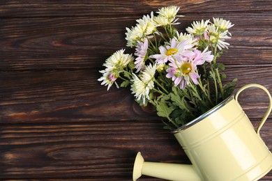 Photo of Watering can with flowers on wooden table, top view. Space for text