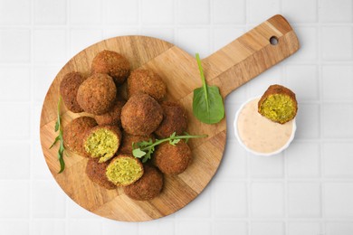 Delicious falafel balls, herbs and sauce on white tiled table, top view