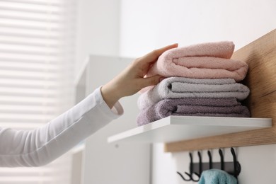 Woman stacking clean towels on shelf indoors, closeup