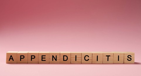 Photo of Word Appendicitis made of wooden cubes with letters on pink background