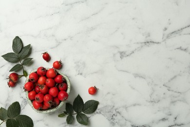 Photo of Ripe rose hip berries with green leaves on white marble table, flat lay. Space for text