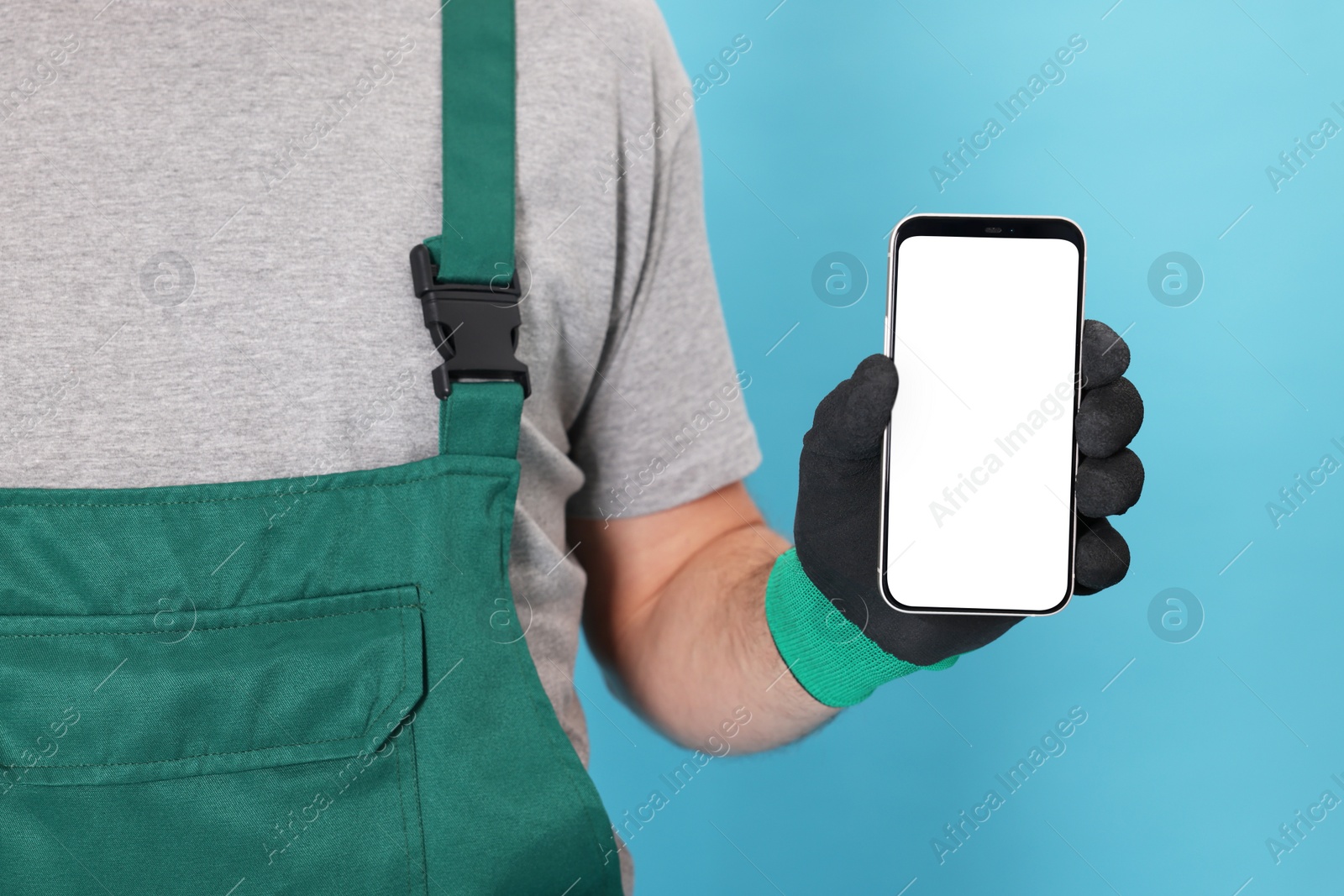 Photo of Professional repairman in uniform with phone on light blue background, closeup