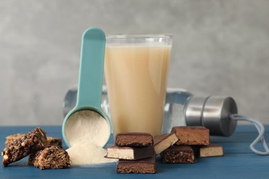 Photo of Different energy bars, water, protein cocktail and powder on blue wooden table