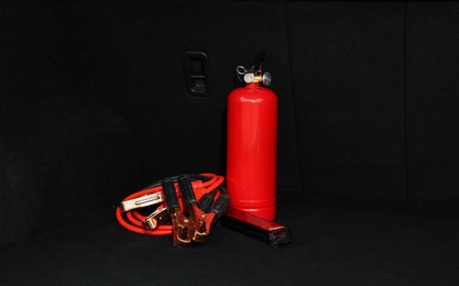 Photo of Red fire extinguisher and battery jumper cables in trunk. Car safety