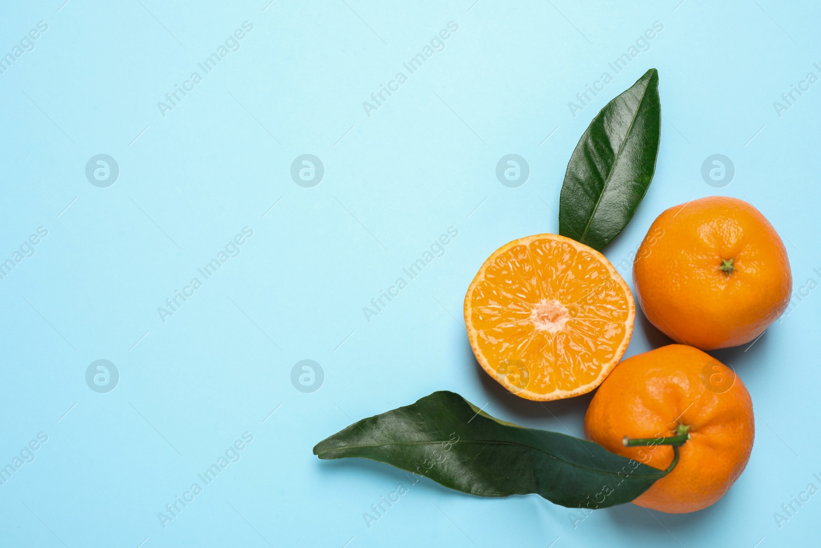 Photo of Flat lay composition with fresh ripe tangerines and leaves on light blue background, space for text. Citrus fruit