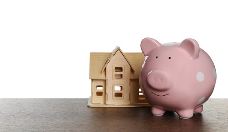 Photo of Piggy bank and house model on wooden table against white background. Saving money concept
