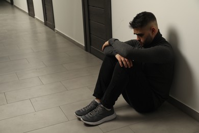 Sad man sitting on floor in hall. Space for text