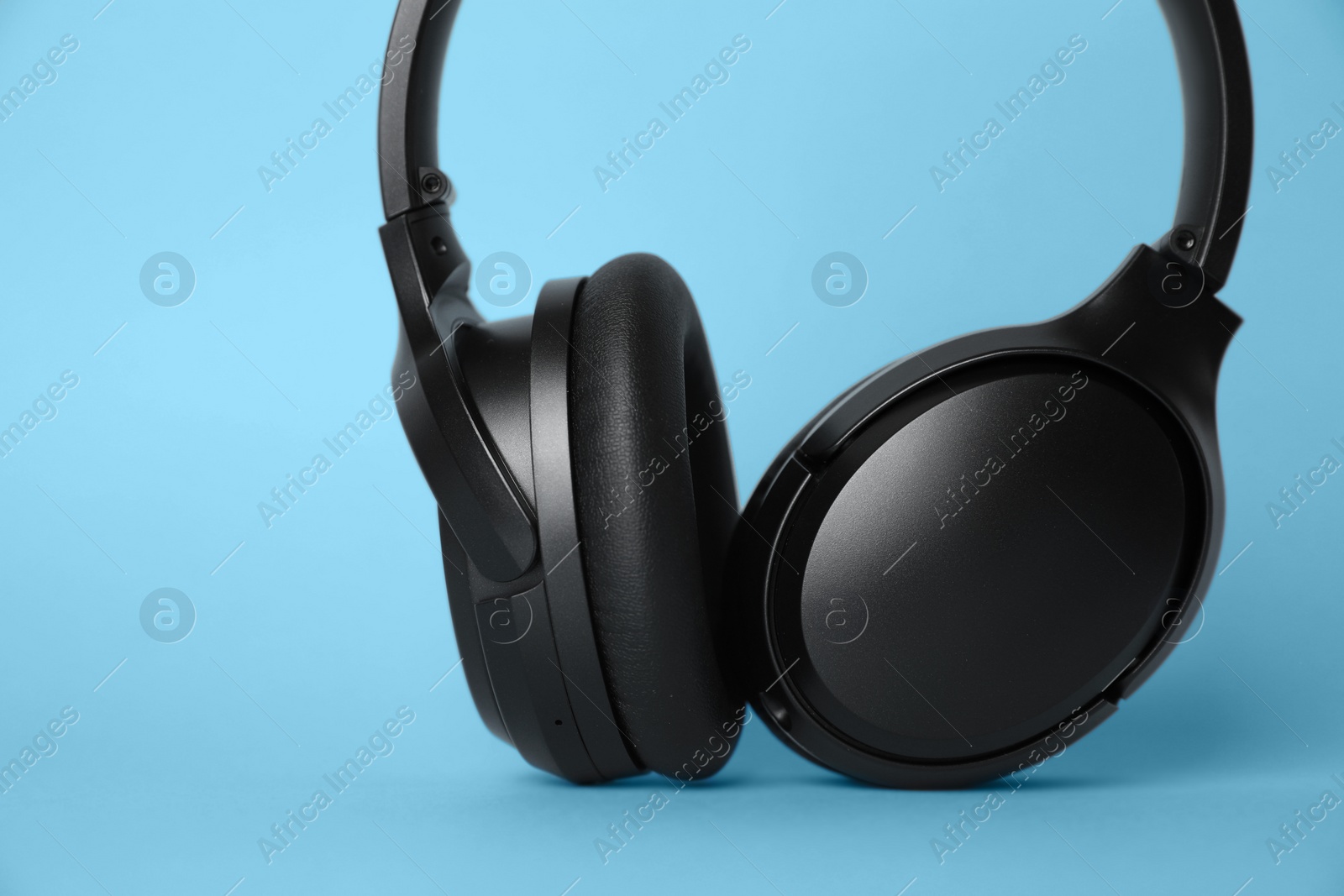 Photo of Modern wireless headphones on light blue background, closeup