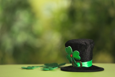 Photo of Leprechaun hat and clover leaves on table against blurred background, space for text. St Patrick's Day celebration