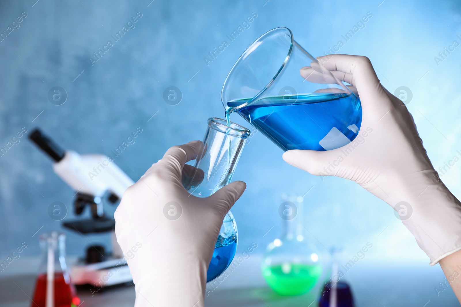 Photo of Assistant pouring sample into glass flask in chemistry laboratory, closeup