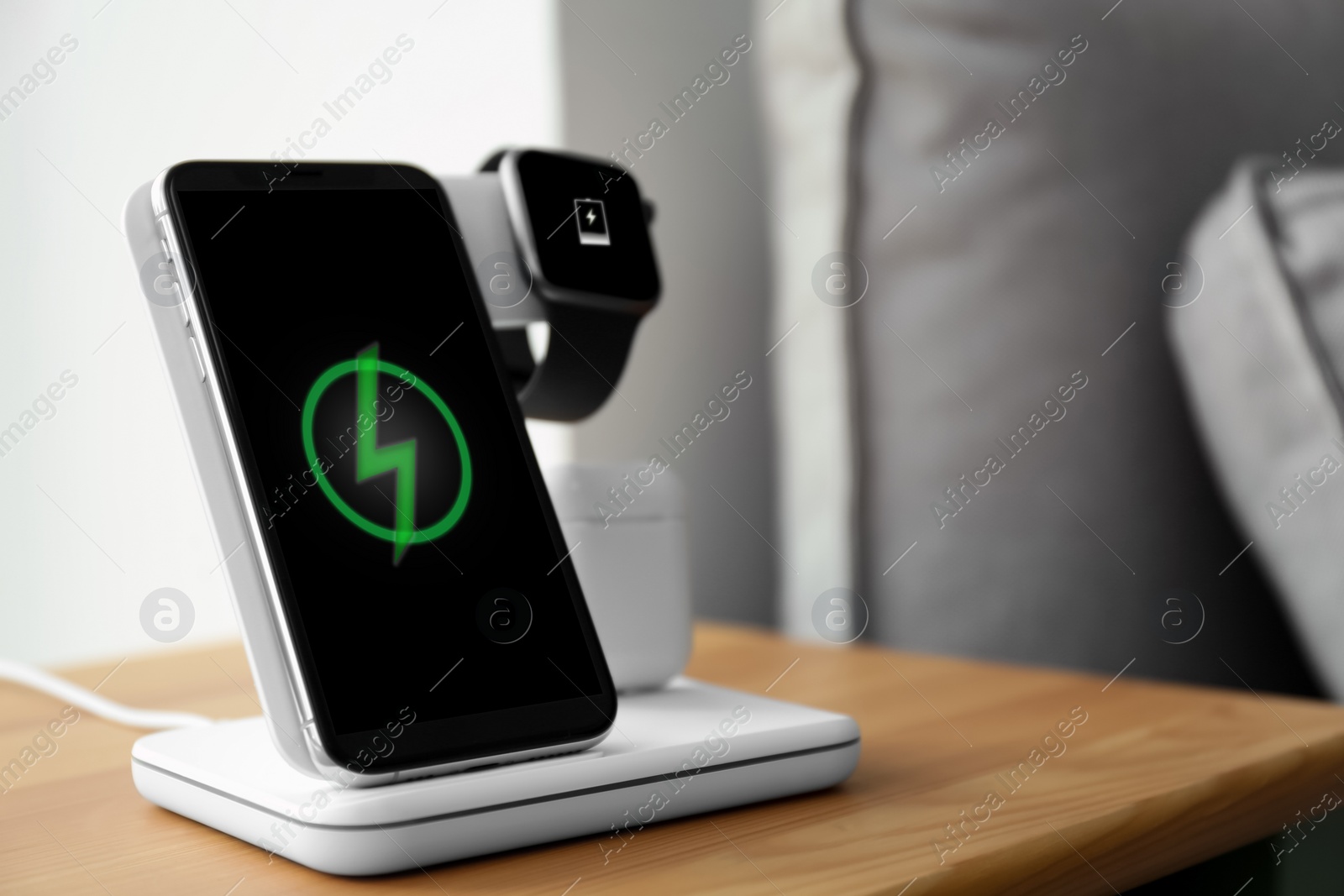 Photo of Smartphone, watch and earphones charging on wireless pad in room. Space for text